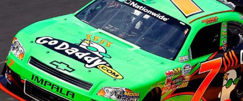 A bright green Chevrolet Impala stock car, featuring "GoDaddy.com" logos, competes in a race. The number 7 is prominently displayed on the hood and sides. Adorned with various sponsorship decals, the car zooms at high speed on the track—a thrilling sight for any presentation or slide template.