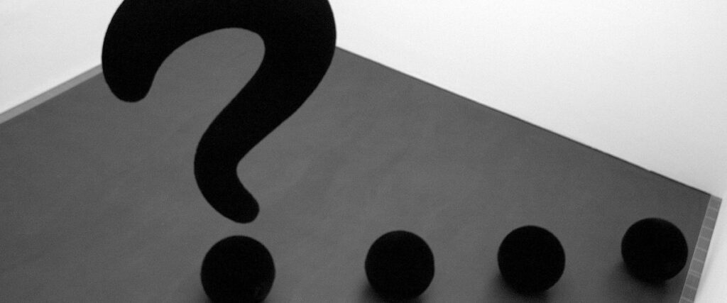 A large black question mark followed by three black dots, each appearing as 3D sculptures, stands on a gray floor next to white walls in a minimalist, possibly art gallery setting. This scene evokes the precision and clarity often sought in a compelling pitch deck.