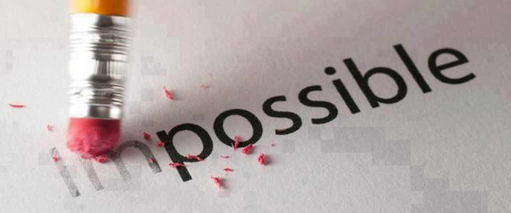 A pencil's eraser is partially erasing the letters "im" from the word "impossible" on a piece of paper, transforming it into the word "possible." Pink eraser shavings are scattered beside the eraser, illustrating a powerful concept perfect for a PowerPoint slide.