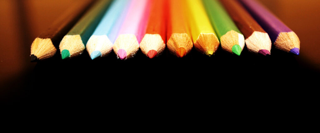 A row of ten sharpened colored pencils arranged side by side with their tips pointing toward the viewer. The pencils are rainbow-colored, starting with red on the left and ending with blue on the right, creating a vibrant gradient effect, perfect for enhancing a colorful PowerPoint presentation.