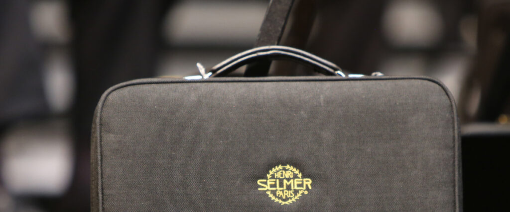 A close-up photo of a black, rectangular musical instrument case with a small silver handle and the Selmer Paris logo printed in yellow on the case. The background is blurred, bringing the focus to the sleek design. This could easily become part of your next pitch deck slide.