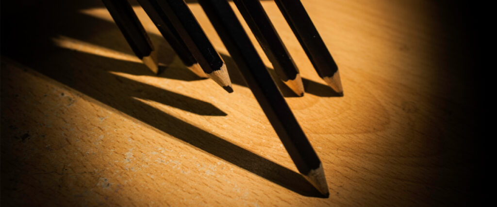 Six black pencils with sharp tips are arranged diagonally on a wooden surface, casting long shadows to the left, creating an interesting interplay of light and shadow. Perfect for enhancing your PowerPoint slide templates effortlessly.