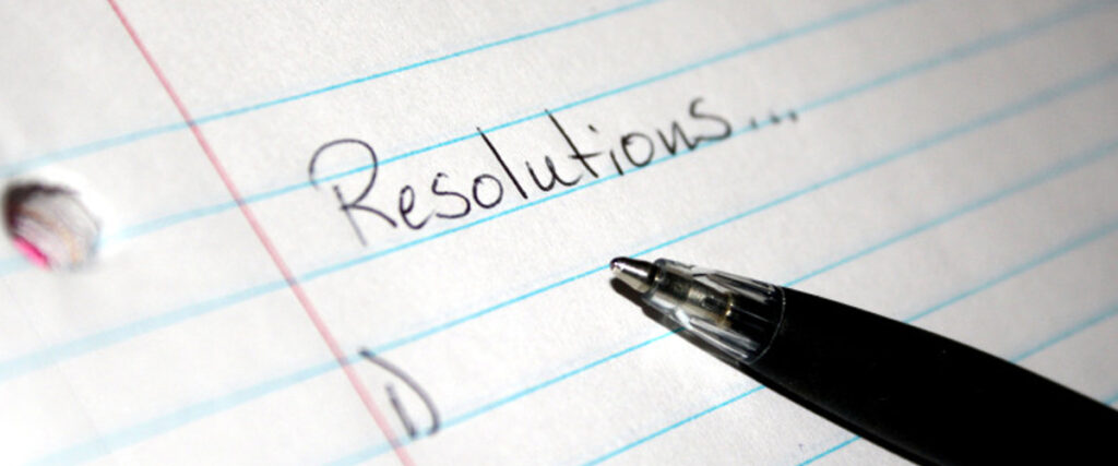 Close-up of a piece of lined notebook paper with a hole on the left side. The word "Resolutions" is handwritten at the top, followed by ellipses. A black pen is placed at the bottom right, pointing towards the text, making it look like a slide template waiting to be filled in.