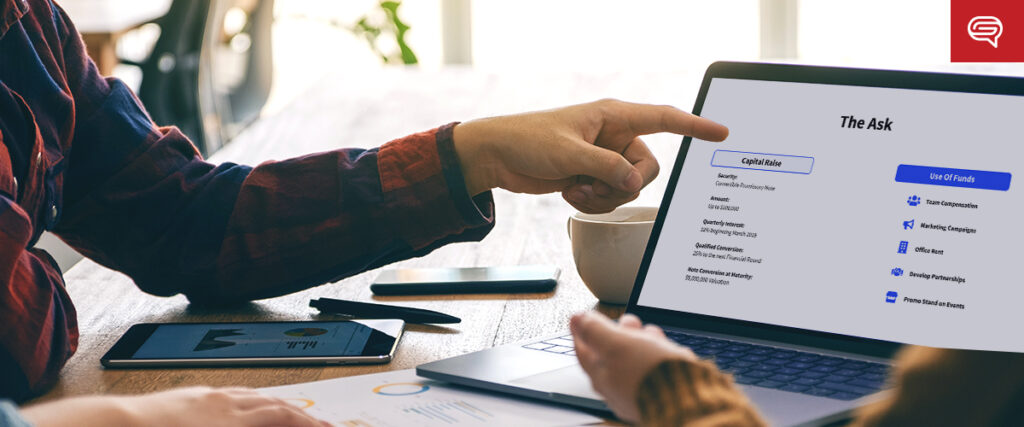 Two people are sitting at a table with a laptop, tablet, and notepads. One person is pointing at a PowerPoint slide template displaying a financial presentation titled "The Ask," including sections for Capital Raise and Use of Funds. They appear to be discussing the content.