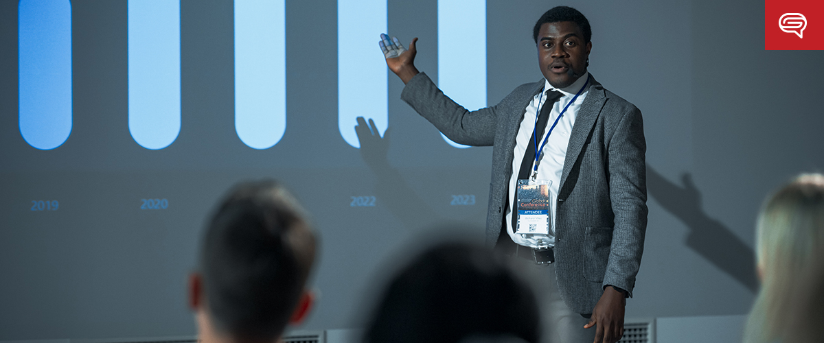 A man in a suit gestures towards a bar graph displayed on a screen during a presentation, reminiscent of flipping through an informative flipbook. He faces an audience seated in front of him, with data from 2019 to 2023 shown on the graph. The room appears to be a professional setting.