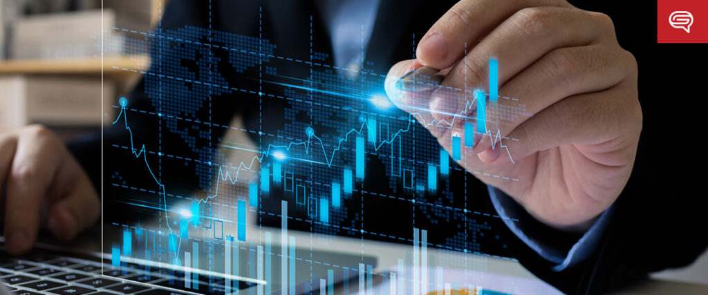 A person in a suit uses a stylus to interact with a digital screen displaying an animated financial chart with rising and falling graphs, and a world map in the background. The blurred background includes a laptop and part of their hand, enhancing their pitch deck presentation.